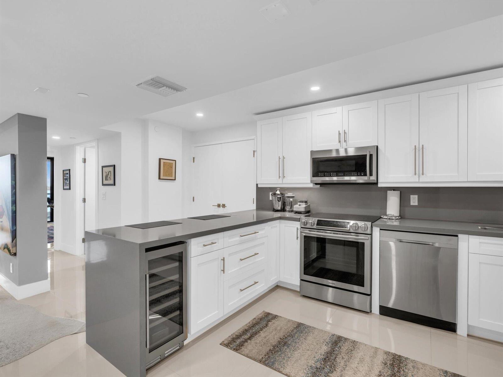 A modern kitchen features white cabinets, gray countertops, stainless steel appliances, and a wine cooler — 3440 S Ocean Boulevard # 307n, Palm Beach FL 33480, PALM BEACH, FL