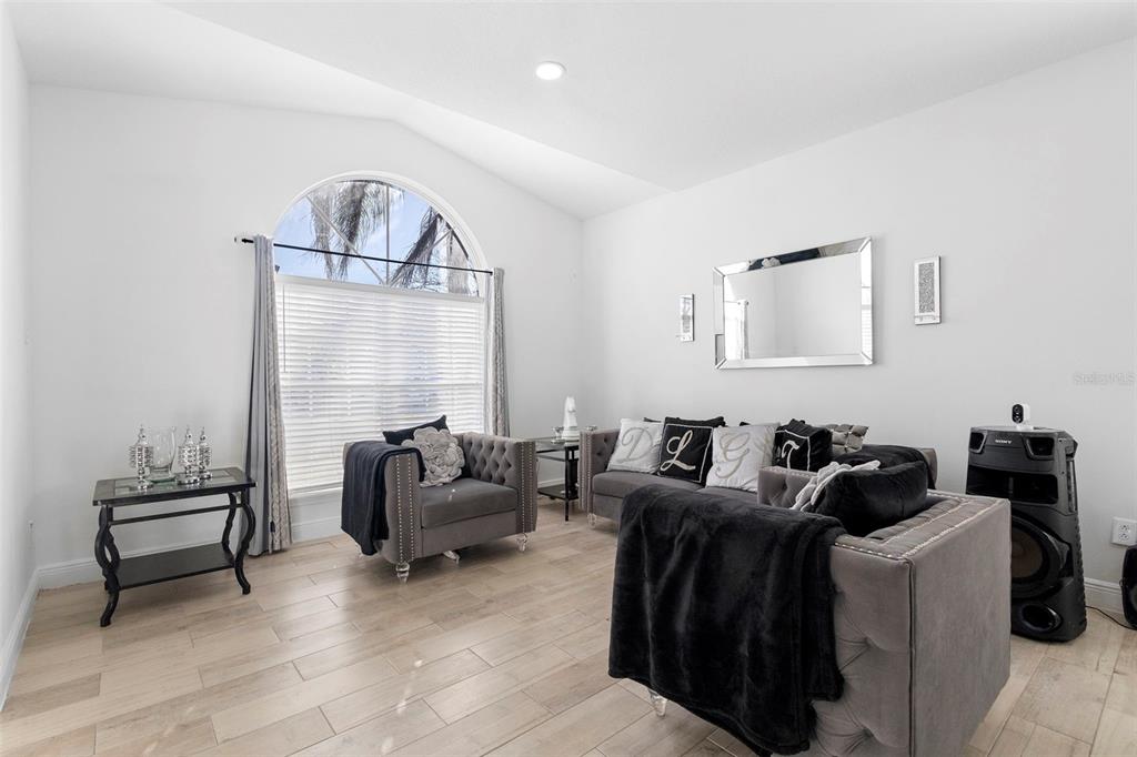 A living room features light wood-look tile flooring, gray tufted furniture, and an arched window — 1739 CANOE CREEK FALLS DRIVE, ORLANDO, FL