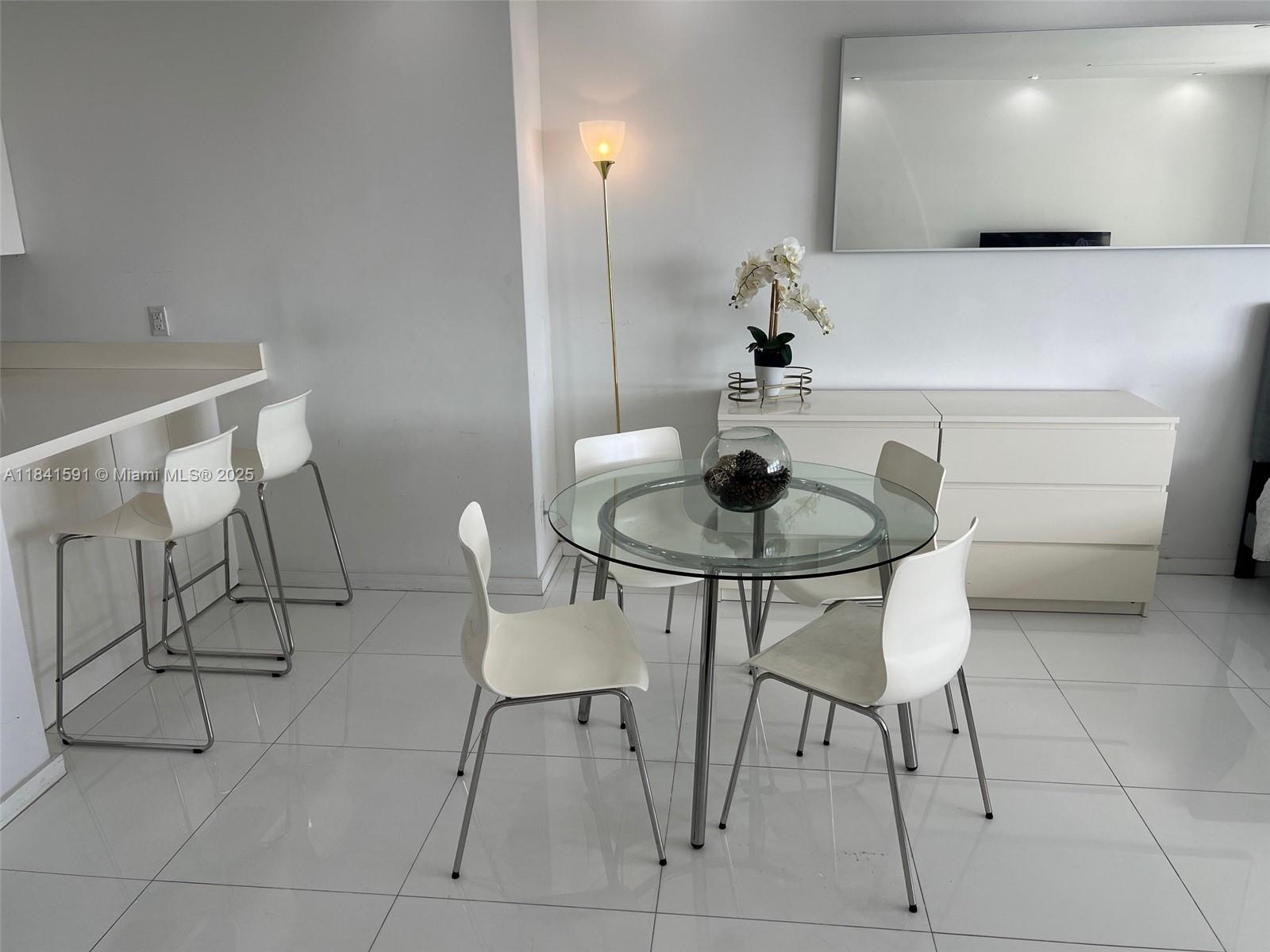 A dining area features a glass table with four white chairs and a white sideboard — 100 Lincoln Rd # 1601, Miami Beach FL 33139, MIAMI BEACH, FL