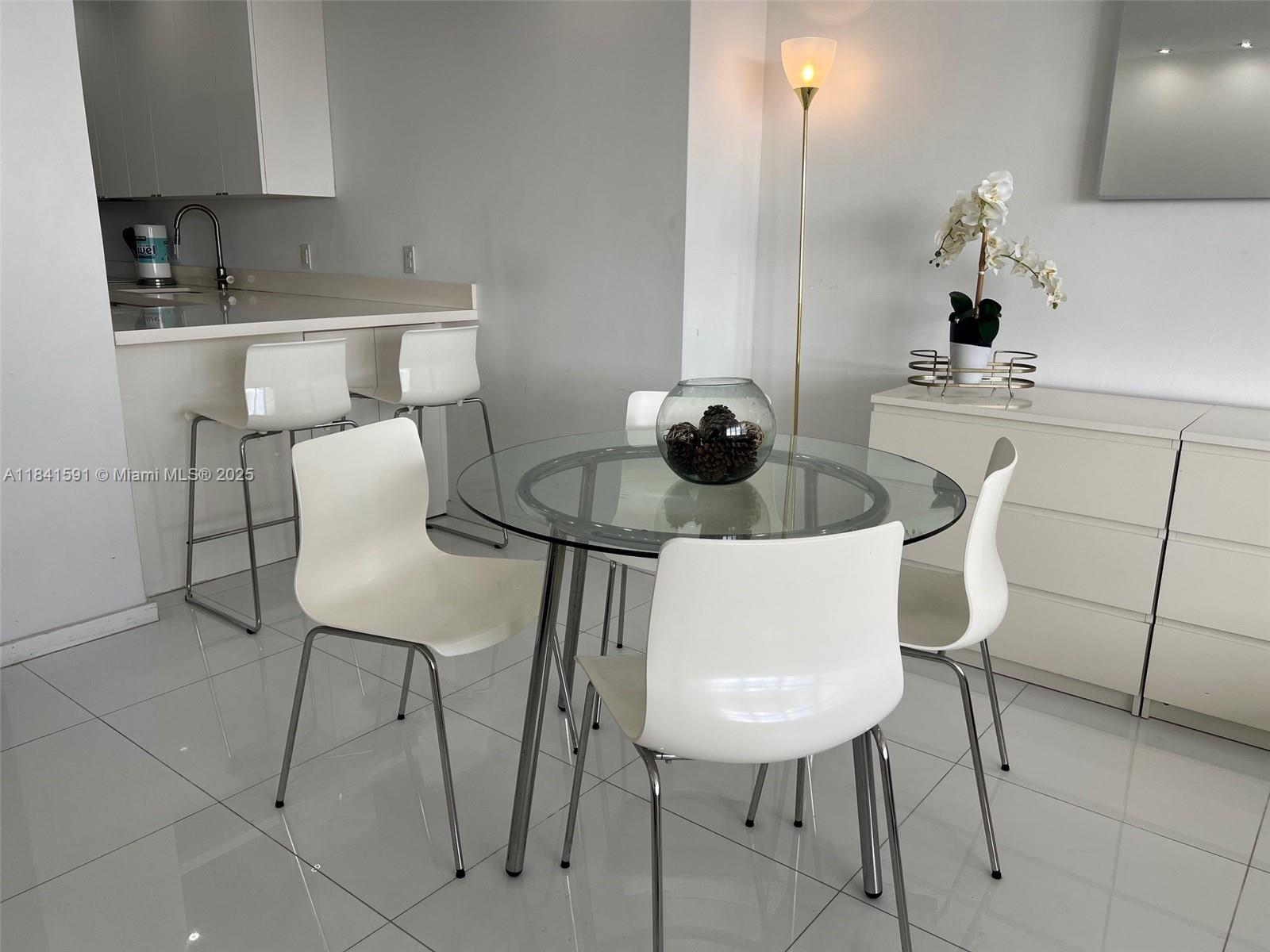 A dining area features a glass-topped table, white chairs, and a kitchen breakfast bar — 100 Lincoln Rd # 1601, Miami Beach FL 33139, MIAMI BEACH, FL