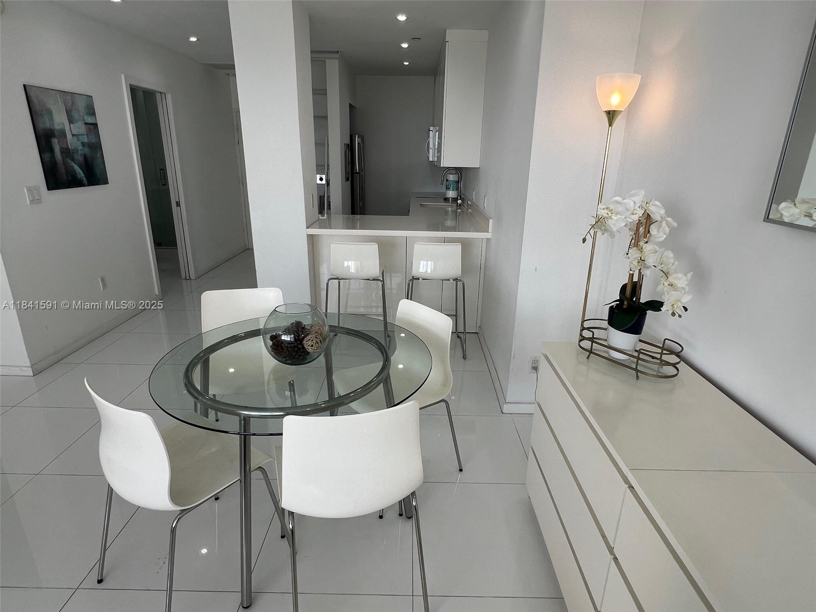 A dining area with a glass table and white chairs sits adjacent to a kitchen — 100 Lincoln Rd # 1601, Miami Beach FL 33139, MIAMI BEACH, FL