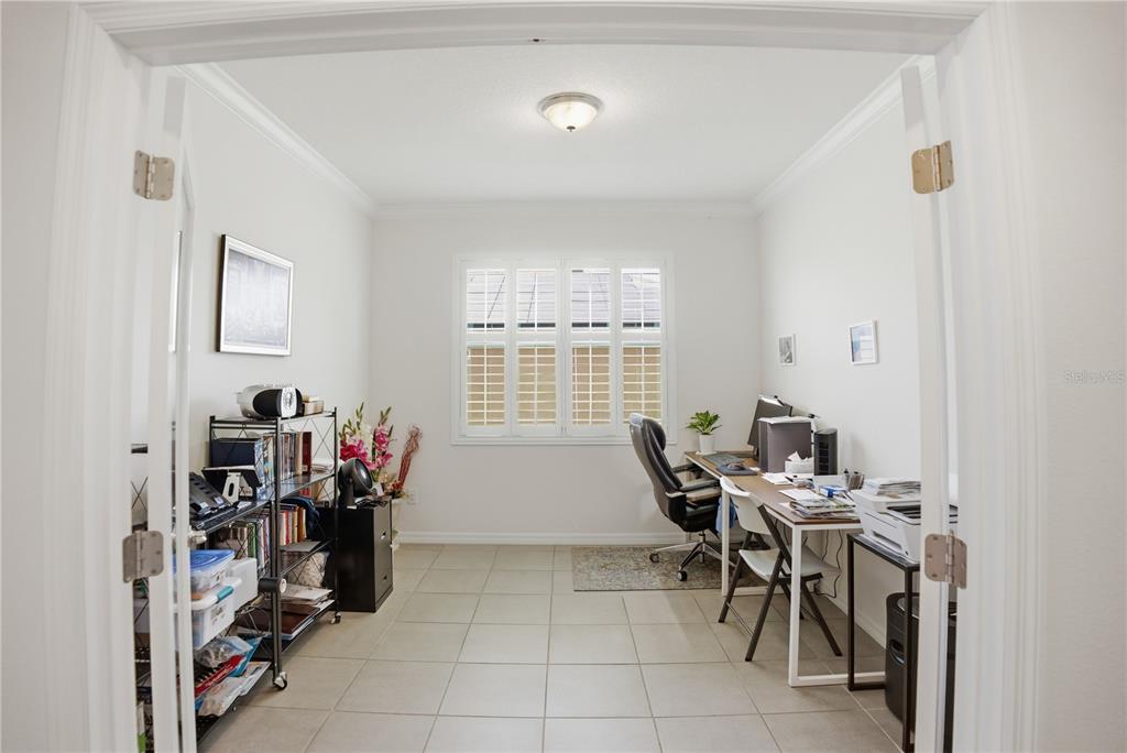 A home office with tile flooring, a desk, a shelving unit, and plantation shutters — 9152 SW 60TH COURT ROAD, OCALA, FL