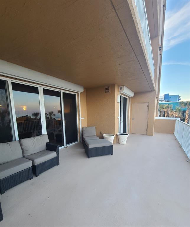 A spacious balcony features wicker furniture, sliding glass doors, and a beige exterior wall — 711 S ATLANTIC AVENUE Unit 202, NEW SMYRNA BEACH, FL