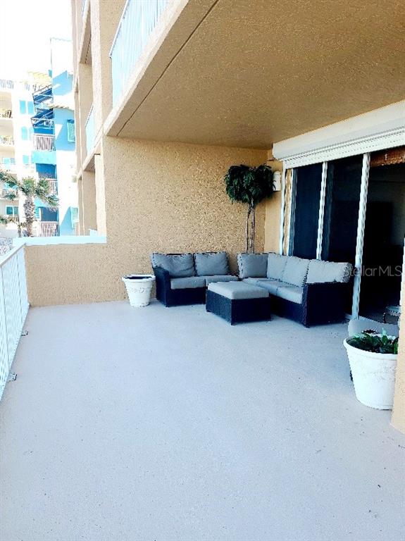 A spacious balcony features outdoor wicker furniture, potted plants, and a view of nearby buildings — 711 S ATLANTIC AVENUE Unit 202, NEW SMYRNA BEACH, FL