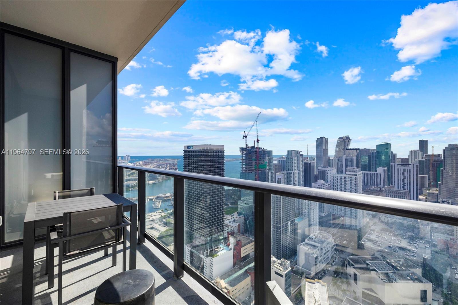 A balcony with outdoor furniture overlooks a dense city skyline and a harbor — 159 NE 6th St # 4910, Miami FL 33132, MIAMI, FL