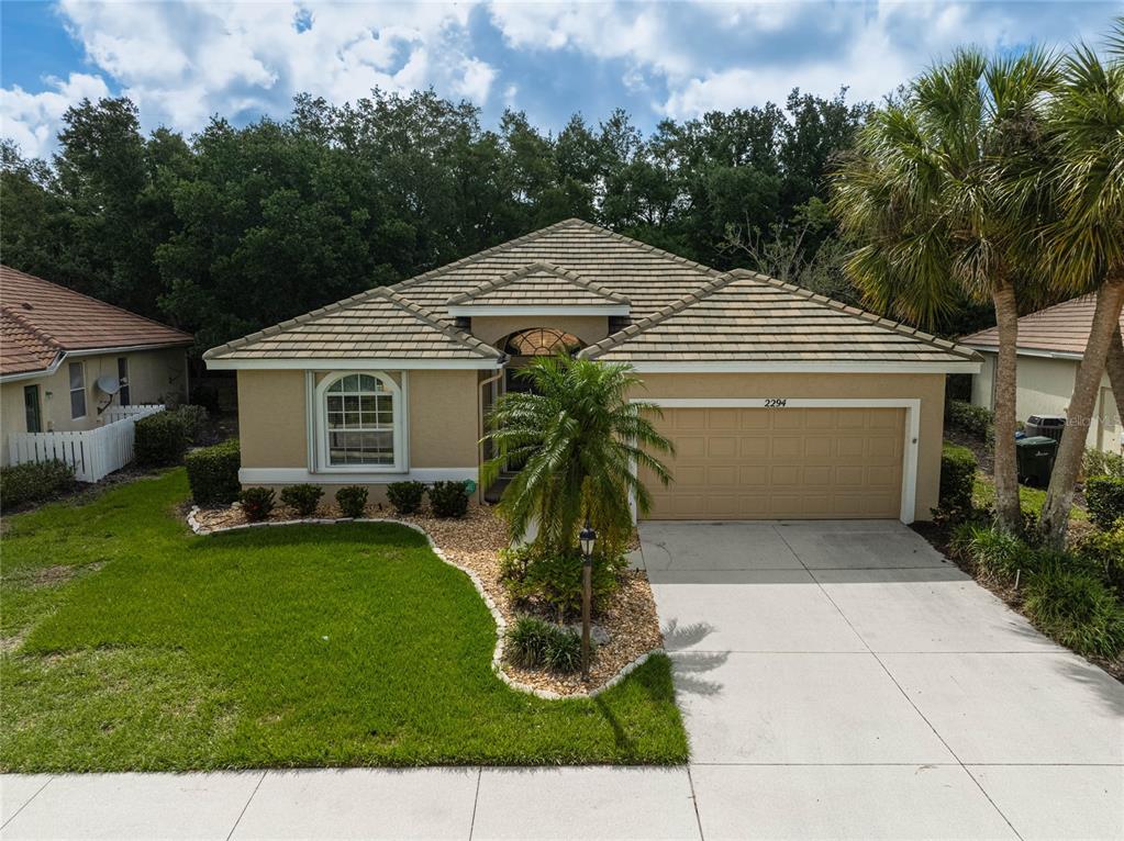 A single-story house with a tan stucco exterior, tile roof, and a two-car garage — 2294 HARRIER WAY, NOKOMIS, FL