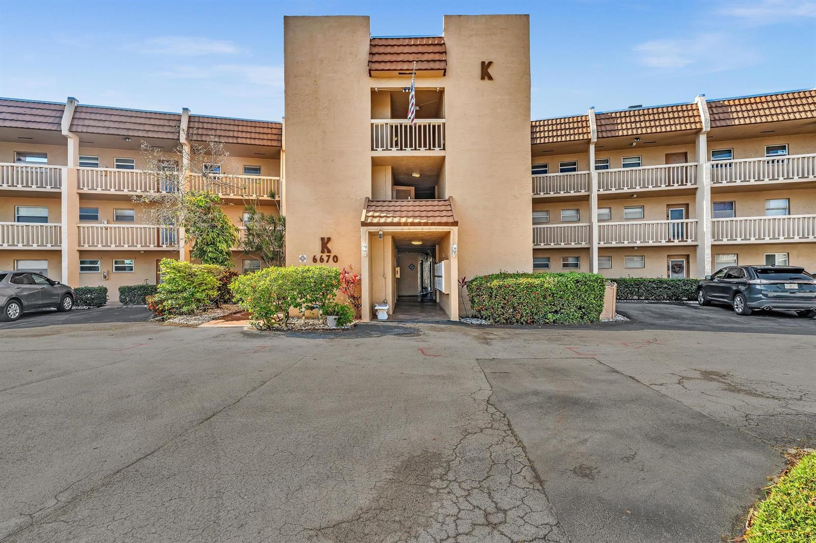 A three-story apartment building exterior features a central entrance with a tan stucco facade — 6670 Royal Palm Boulevard # 110, Margate FL 33063, MARGATE, FL