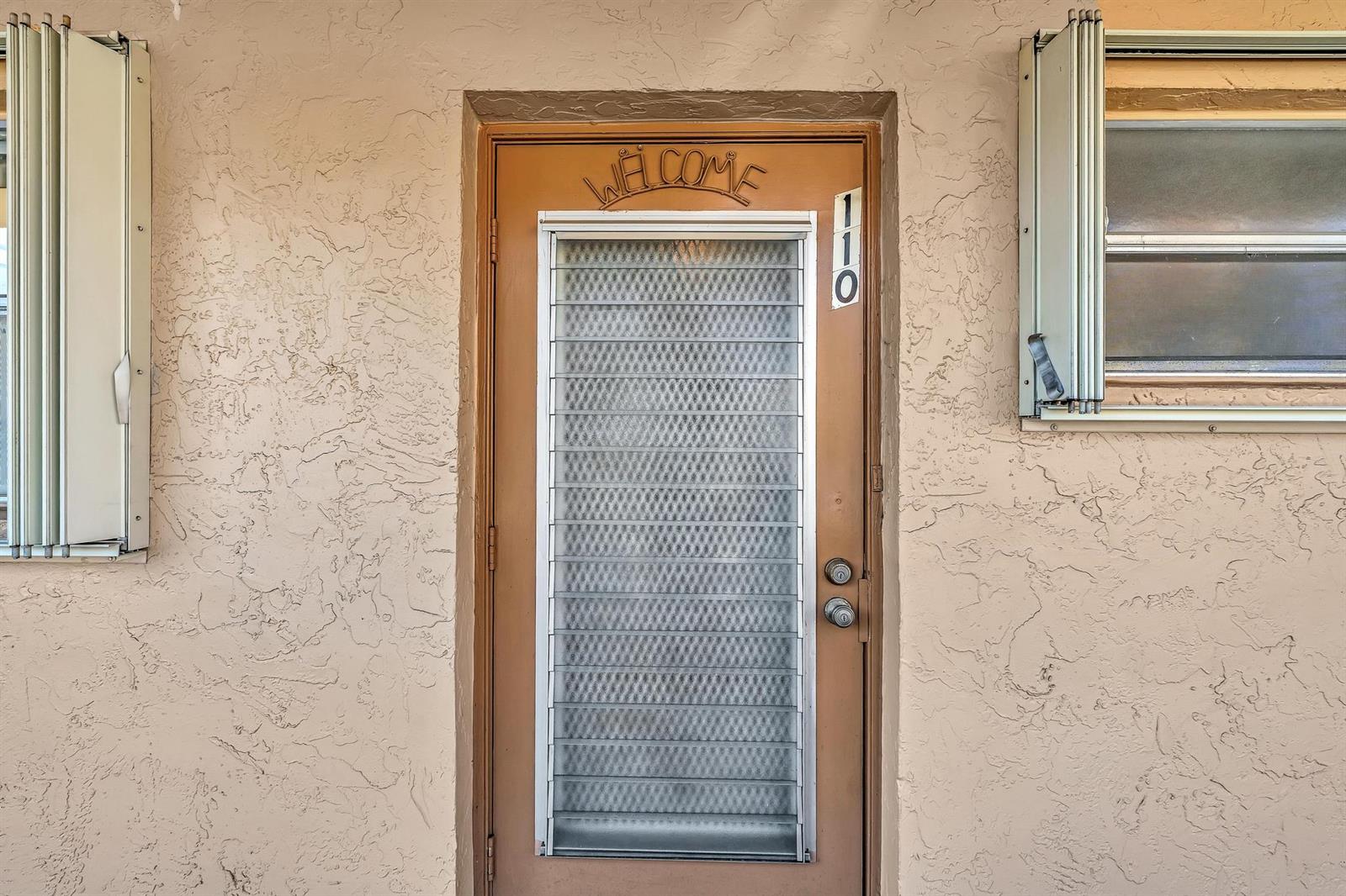 A tan exterior wall features a brown door with a louvered glass insert and address numbers — 6670 Royal Palm Boulevard # 110, Margate FL 33063, MARGATE, FL