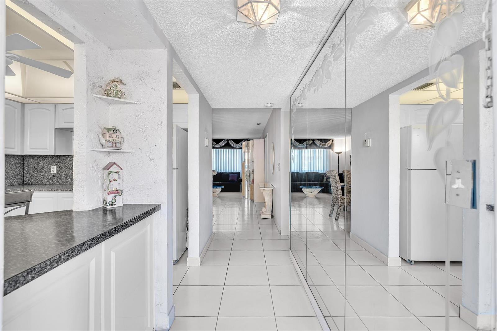 A tiled hallway leads from a kitchen counter toward a living area with mirrored walls — 6670 Royal Palm Boulevard # 110, Margate FL 33063, MARGATE, FL
