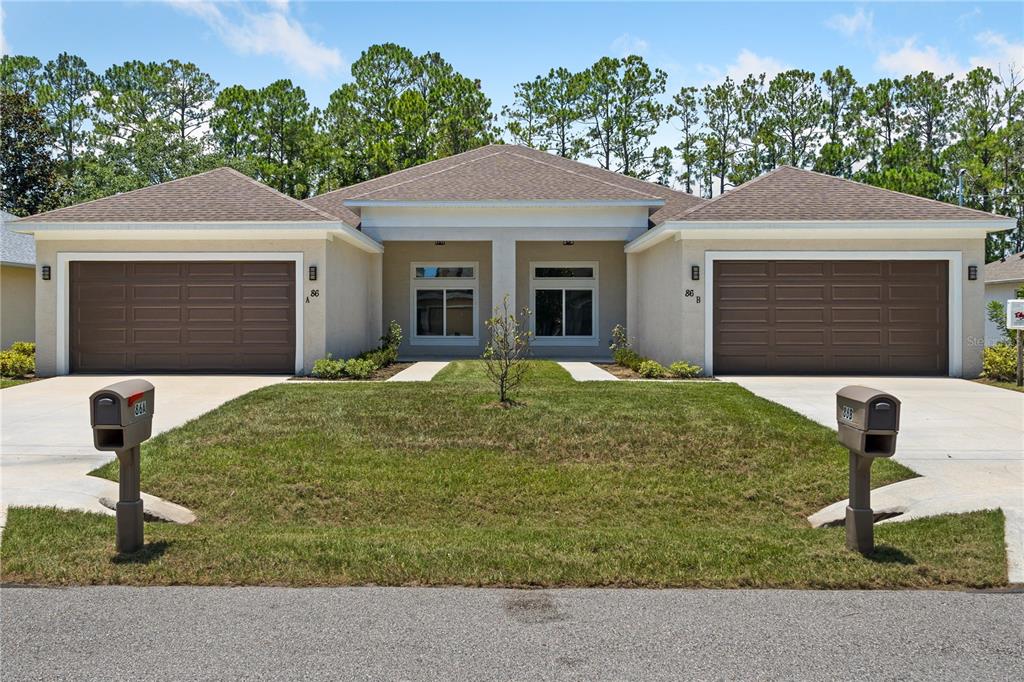 A duplex home with two brown garage doors, beige stucco siding, and a shared lawn — 86 EMERSON DRIVE, PALM COAST, FL