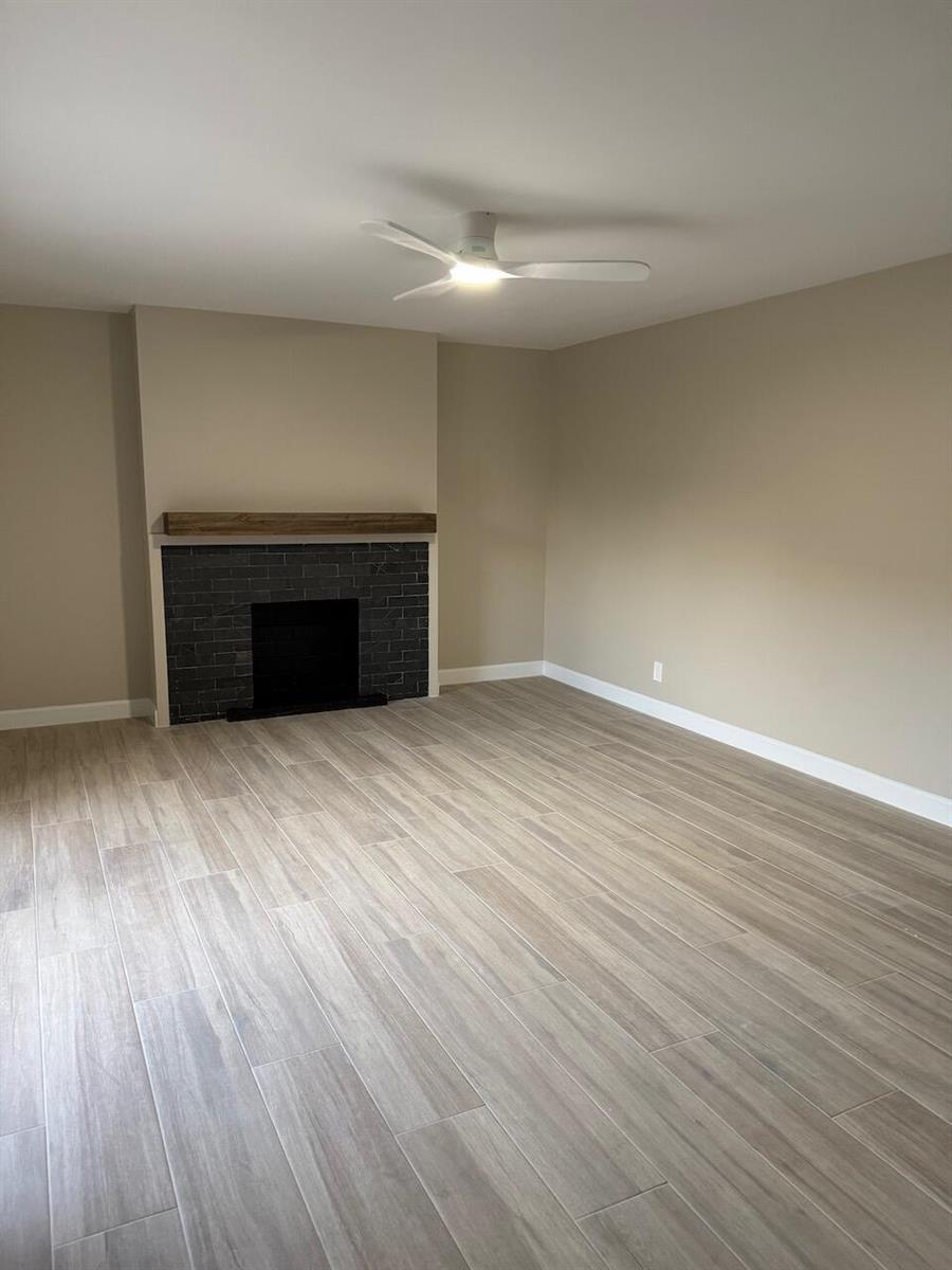 A living room features light wood-look tile flooring, beige walls, and a dark brick fireplace — 79 Lake Arbor Drive # 79, Palm Springs FL 33461, PALM SPRINGS, FL