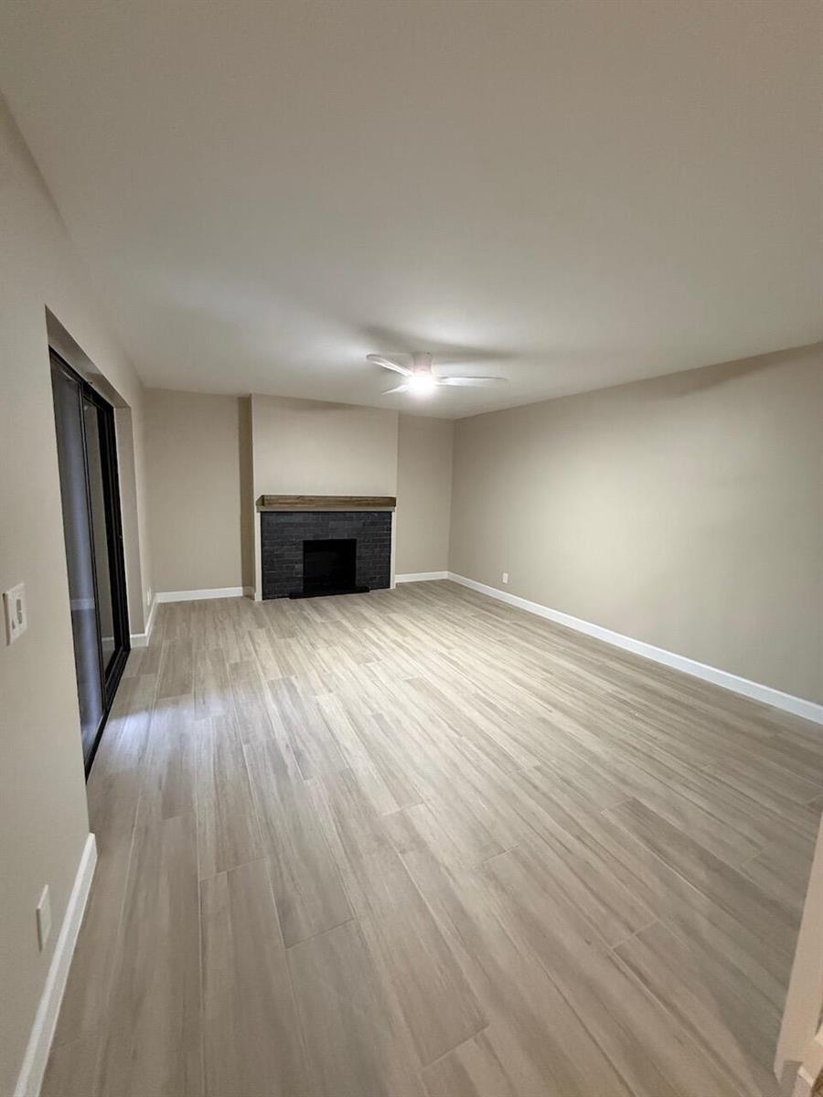 A living room with light wood-look tile flooring, beige walls, and a dark brick fireplace — 79 Lake Arbor Drive # 79, Palm Springs FL 33461, PALM SPRINGS, FL