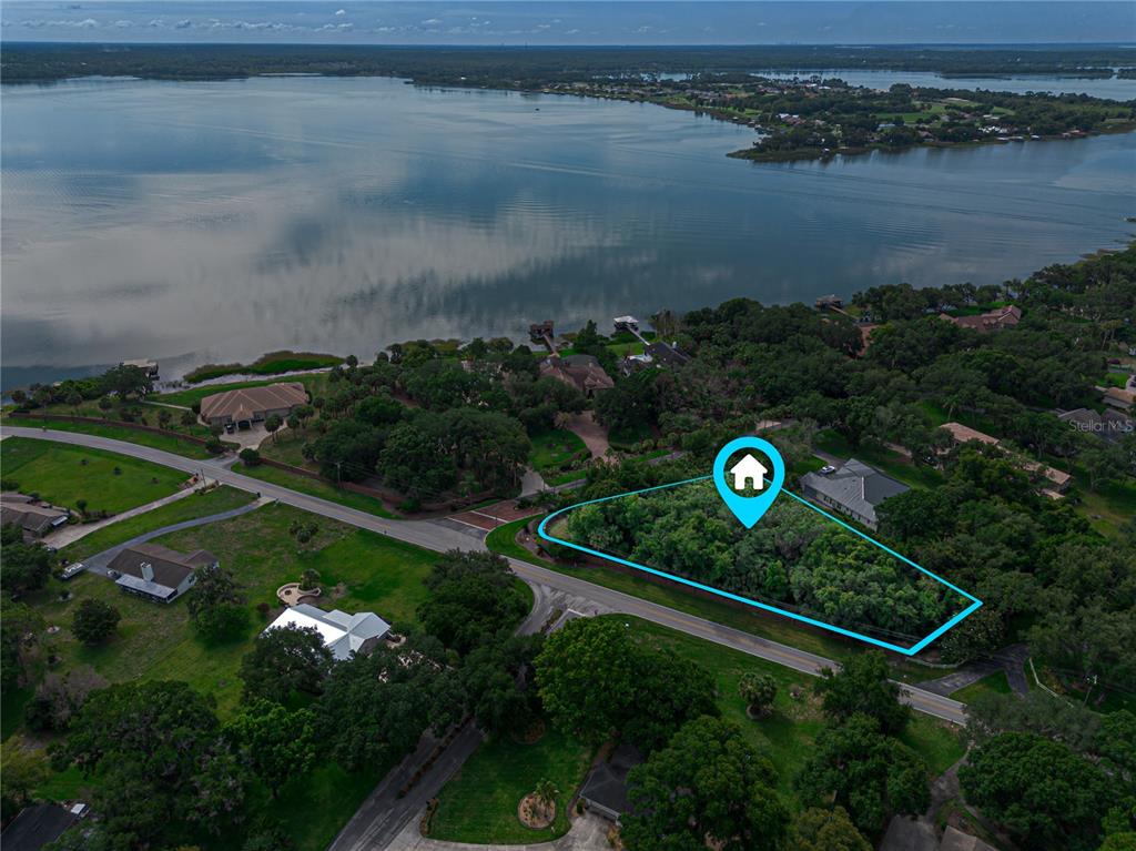 An aerial view shows a wooded, triangular vacant lot bordered by roads near a lake — 000 LAKESHORE POINTE BOULEVARD, MOUNT DORA, FL