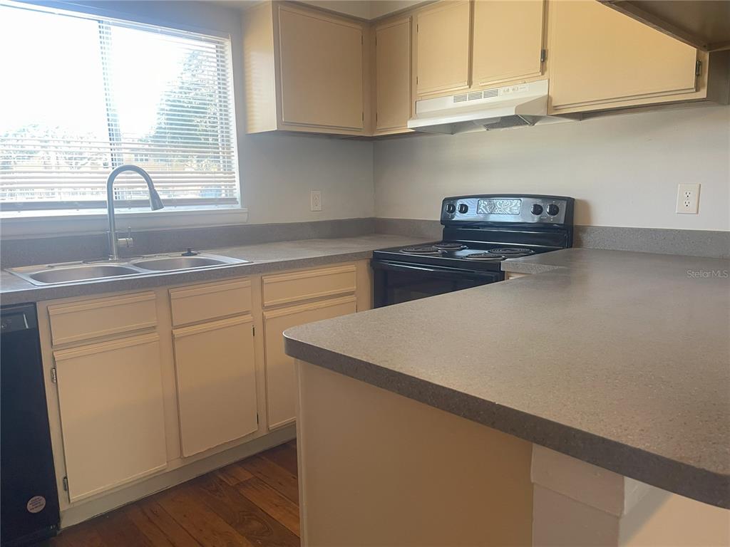 A kitchen features beige cabinets, a black stove, a double sink, and gray countertops — 4419 S SEMORAN BOULEVARD UNIT 7, ORLANDO, FL
