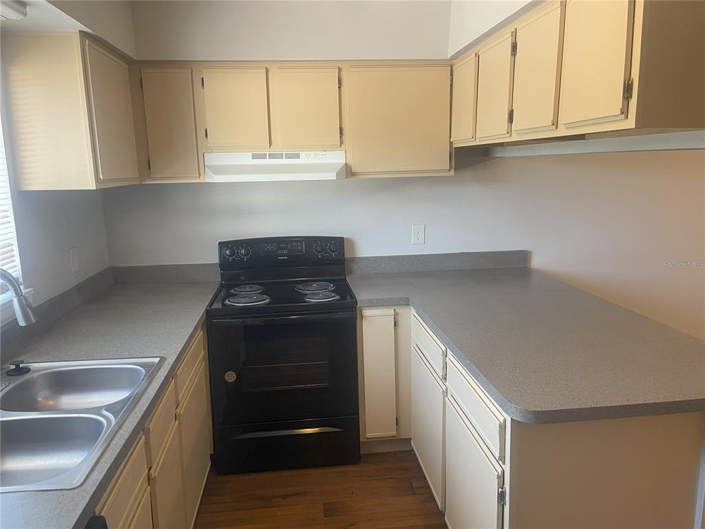 A kitchen features light-colored cabinets, gray countertops, and a black electric stove — 4419 S SEMORAN BOULEVARD UNIT 7, ORLANDO, FL