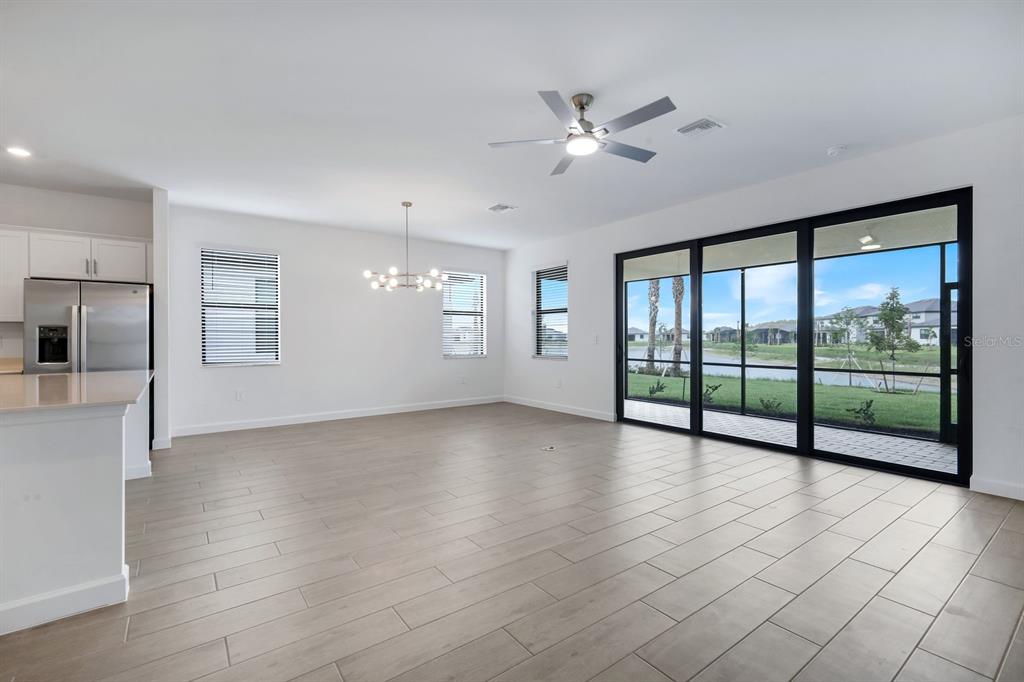 An open-concept living and dining area features light wood-look tile floors and large sliding doors — 19232 GENTRY PLACE, ESTERO, FL