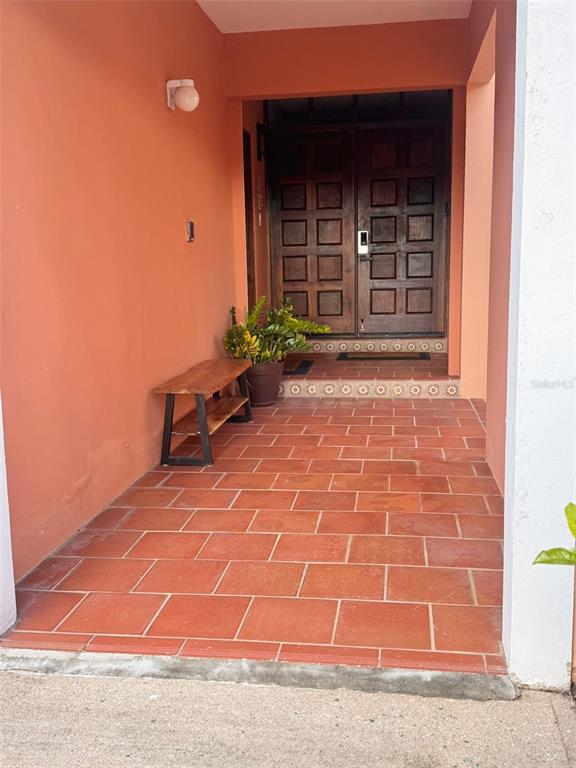 A covered entryway features terracotta tile flooring, a wooden bench, and double wooden front doors — Fairway Courts FAIRWAY COURTS UNIT 828, HUMACAO, PR