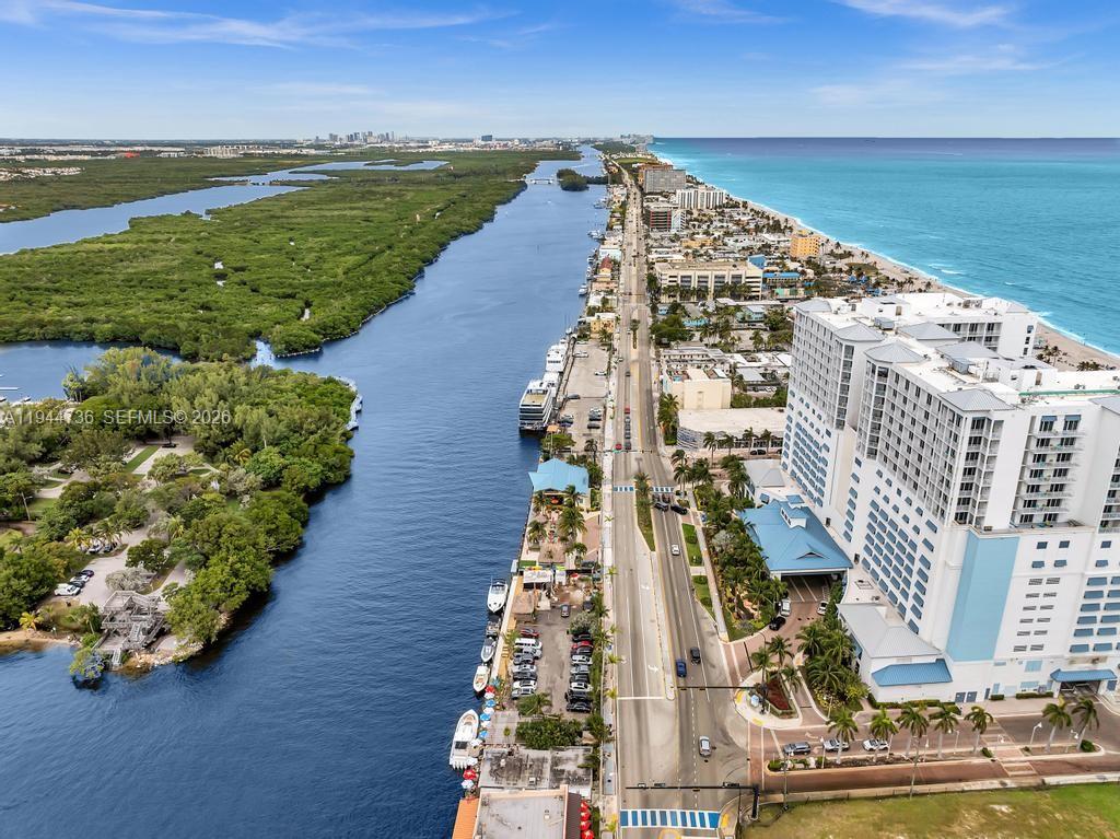 An aerial view shows a coastal road separating a waterway from high-rise buildings and beach — 1318 N Ocean Dr, Hollywood FL 33019, HOLLYWOOD, FL
