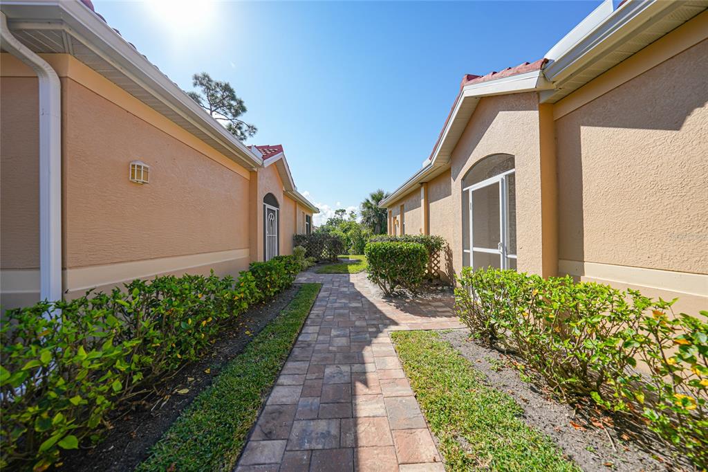 A paved walkway leads between two tan stucco houses with green hedges and screen doors — 3810 COBIA VILLAS COURT, PUNTA GORDA, FL
