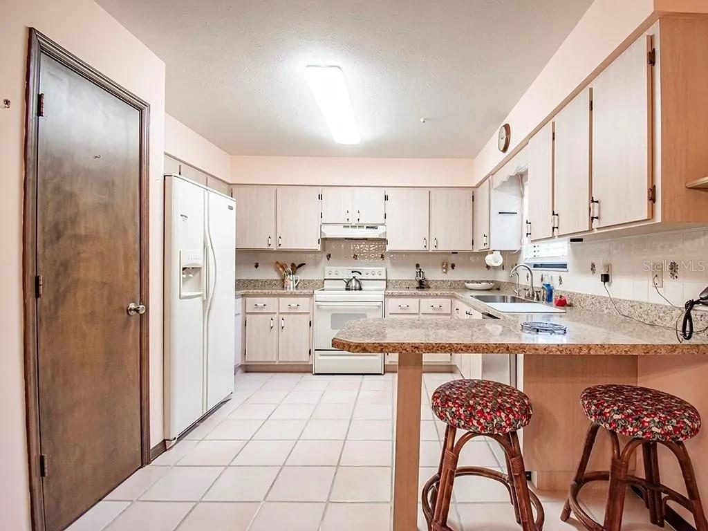 A kitchen features light wood cabinets, white appliances, tile flooring, and a granite-topped breakfast bar — 7101 NORTH BOULEVARD, FORT PIERCE, FL