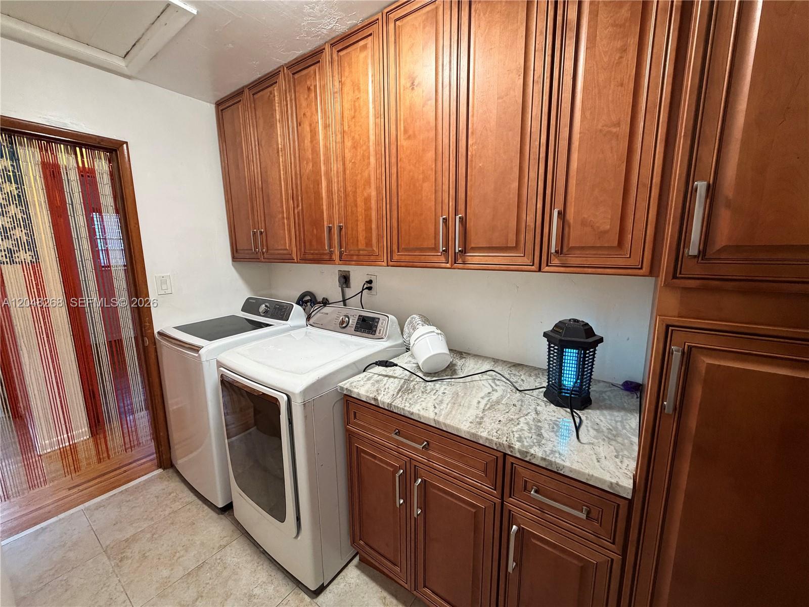 A laundry room features wooden cabinets, granite countertops, and a side-by-side washer and dryer — 45 SE 14th St, Dania Beach FL 33004, DANIA BEACH, FL