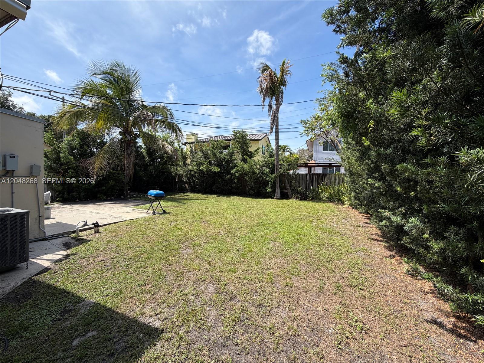 A grassy backyard features a concrete patio, palm trees, and a small charcoal grill — 45 SE 14th St, Dania Beach FL 33004, DANIA BEACH, FL