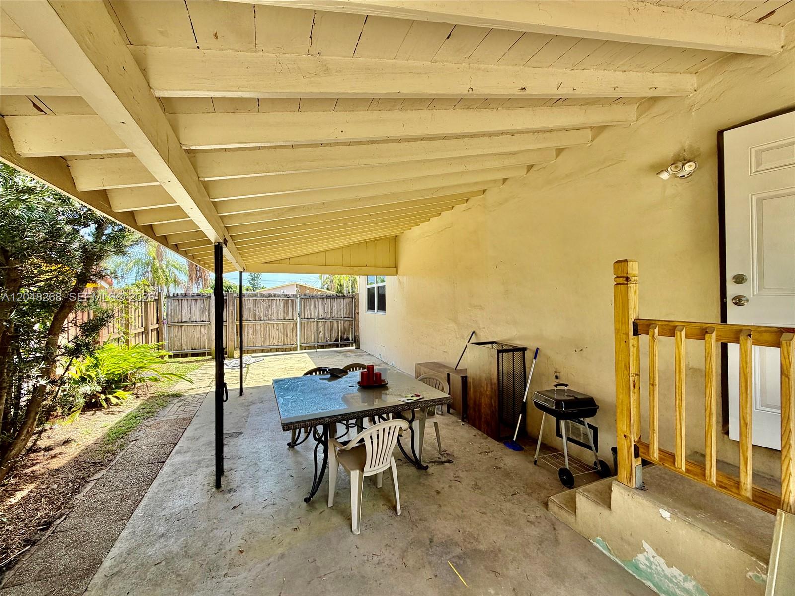 A covered concrete patio features a dining table, chairs, and a small charcoal grill — 45 SE 14th St, Dania Beach FL 33004, DANIA BEACH, FL