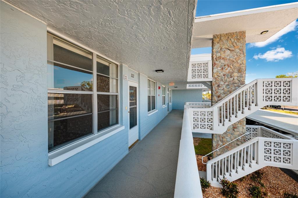 An exterior walkway leads to a unit door with a stone pillar and white staircase — 4715 BAY STREET NE UNIT 222, ST PETERSBURG, FL