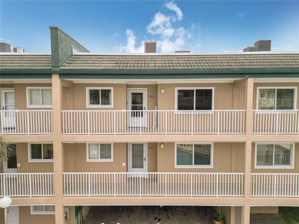 An exterior view of a multi-story apartment building with balconies and tan vertical siding — 150 HARBORSIDE AVENUE UNIT 307, PUNTA GORDA, FL
