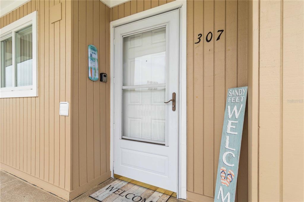 The exterior entrance of a residence features a white storm door and a welcome sign — 150 HARBORSIDE AVENUE UNIT 307, PUNTA GORDA, FL