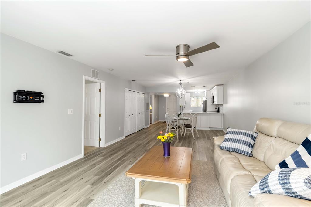 A living room with light wood-look flooring, a beige sofa, and an open-concept kitchen beyond — 150 HARBORSIDE AVENUE UNIT 307, PUNTA GORDA, FL