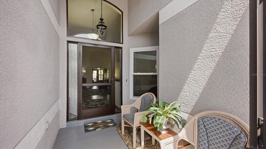 A covered entryway features a glass-paneled front door, two wicker chairs, and a small table — 1834 E DEL WEBB BOULEVARD, SUN CITY CENTER, FL