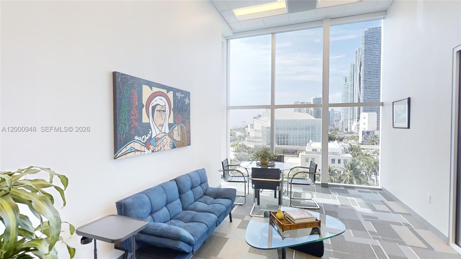 A modern office lounge features a blue sofa, glass coffee table, and floor-to-ceiling city views — 1501 Biscayne Blvd # C1, Miami FL 33132, MIAMI, FL