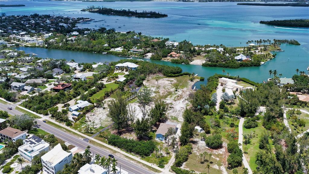 An aerial view shows a vacant waterfront lot surrounded by trees, houses, and a road — 6664 & 6660 & 6670 GULF OF MEXICO DRIVE, LONGBOAT KEY, FL