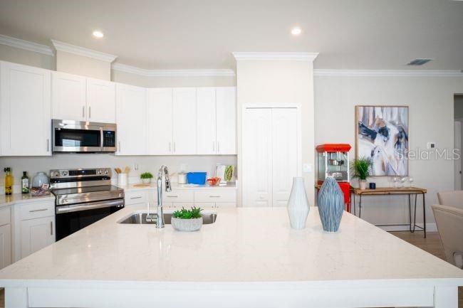 A bright kitchen features white cabinets, a large quartz island, and stainless steel appliances — 3864 BLUETHREAD WAY, POINCIANA, FL