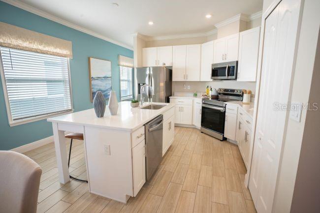 A kitchen with white cabinets, stainless steel appliances, a center island, and light wood-look flooring — 3864 BLUETHREAD WAY, POINCIANA, FL