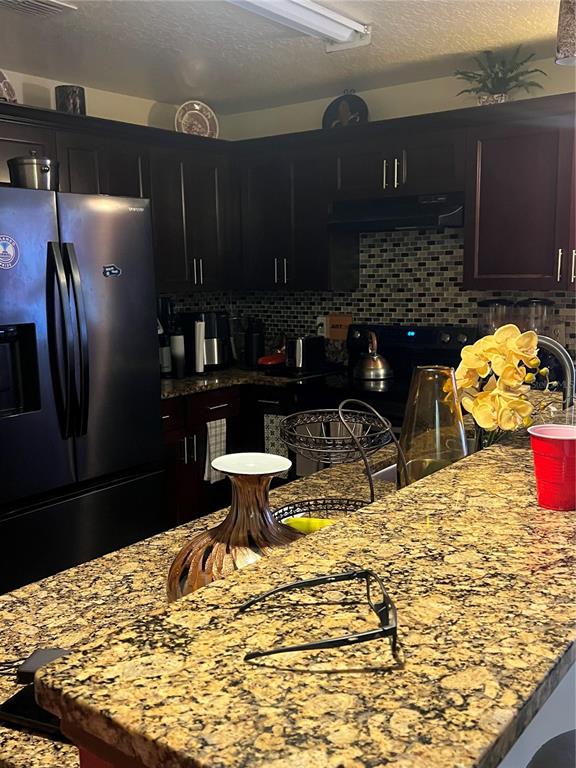 A kitchen features dark wood cabinets, granite countertops, and a black refrigerator — 4252 PAPPY KENNEDY STREET, ORLANDO, FL