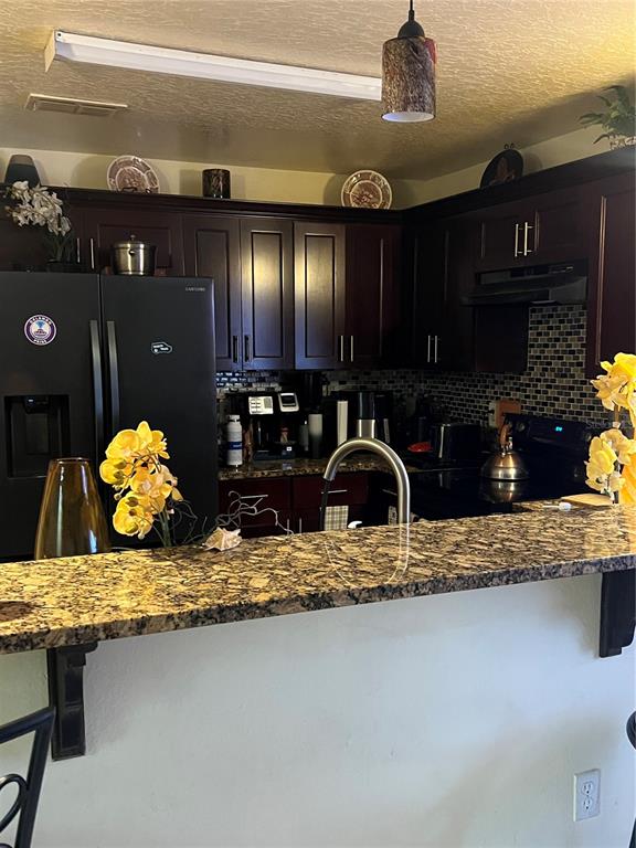 A kitchen features dark wood cabinets, granite countertops, a black refrigerator, and a mosaic backsplash — 4252 PAPPY KENNEDY STREET, ORLANDO, FL