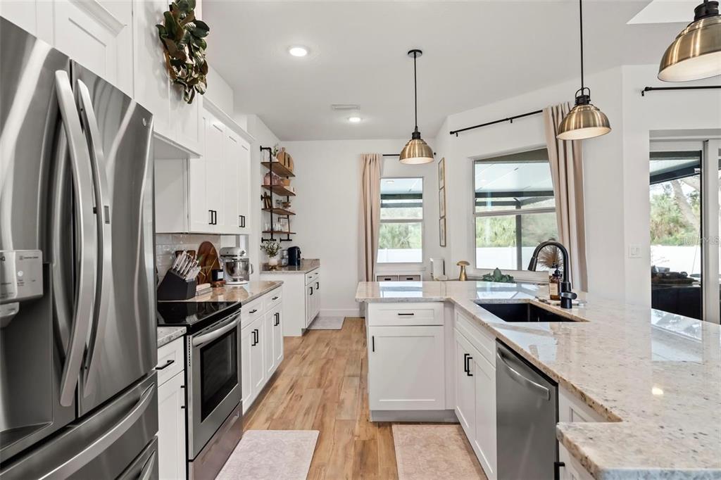 A kitchen features a granite-topped island with bar stools, stainless steel appliances, and pendant lighting — 8233 GIVLIC LANE, NORTH PORT, FL