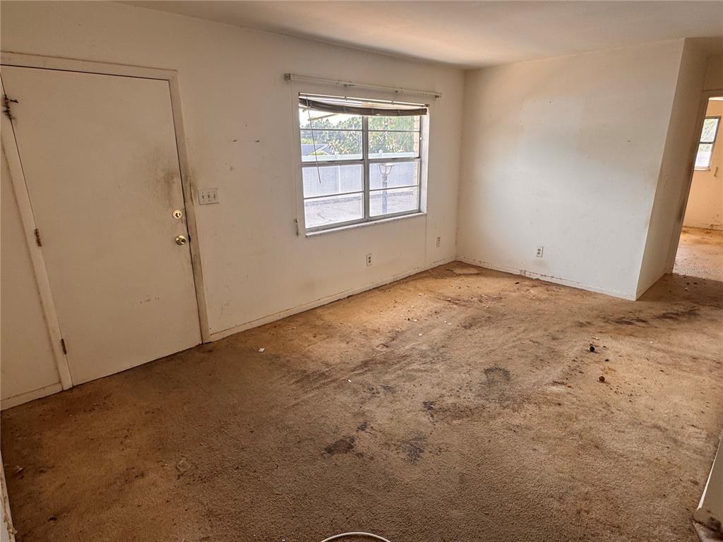 An empty room with stained, worn carpeting, a white door, and a single window — 12400 PARK BOULEVARD UNIT 625, SEMINOLE, FL
