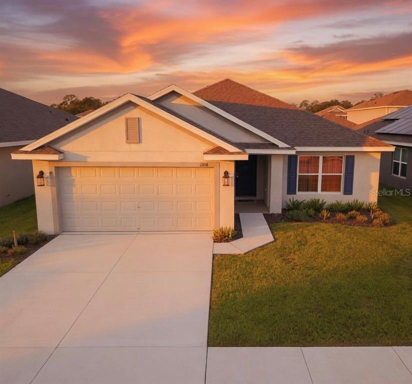 A single-story suburban house with a two-car garage and a sunset sky background — 2108 CARTGATE LANE, WINTER HAVEN, FL