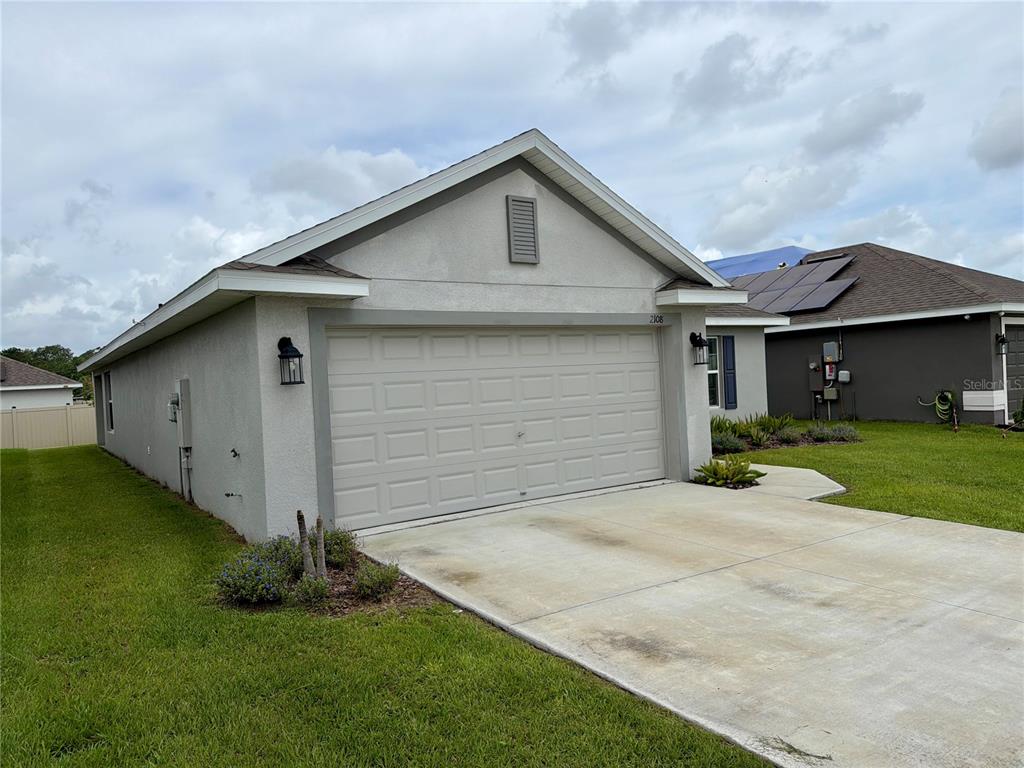 A single-story house exterior with a two-car garage, stucco siding, and a concrete driveway — 2108 CARTGATE LANE, WINTER HAVEN, FL