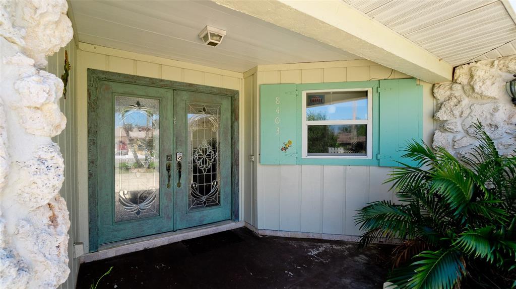 A front entryway features a double glass door, a window with teal shutters, and stone siding — 8403 13TH AVENUE NW, BRADENTON, FL
