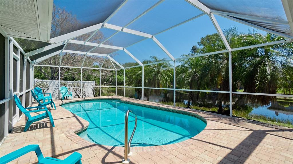 A screened-in swimming pool with a brick paver deck overlooks a pond and palm trees — 8403 13TH AVENUE NW, BRADENTON, FL