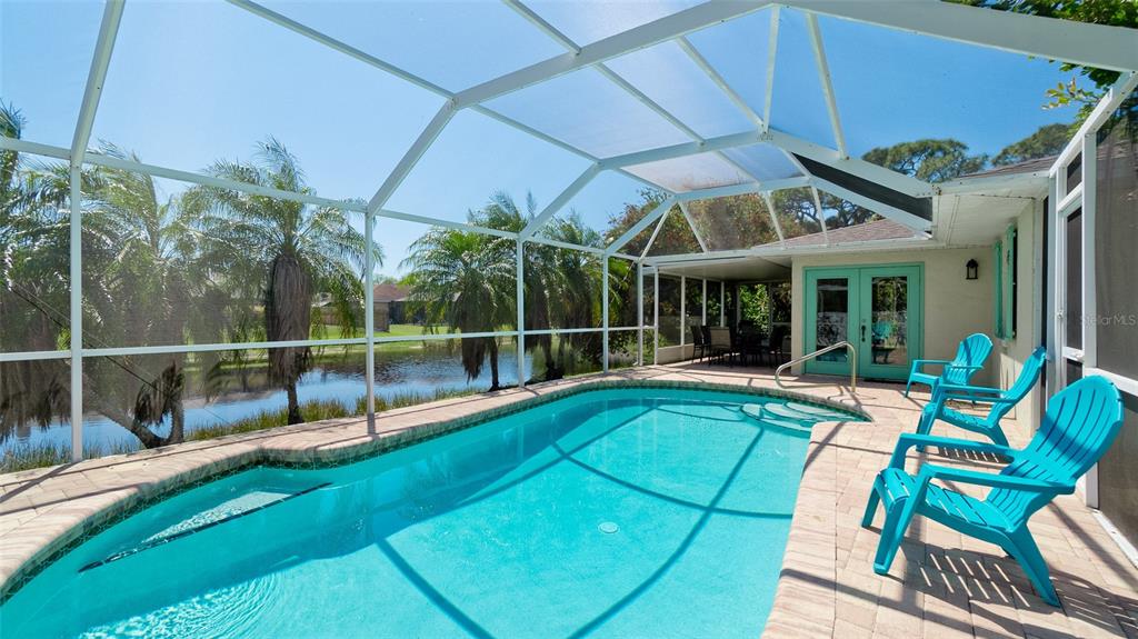 A screened-in swimming pool with a brick deck and bright blue chairs overlooks a pond — 8403 13TH AVENUE NW, BRADENTON, FL