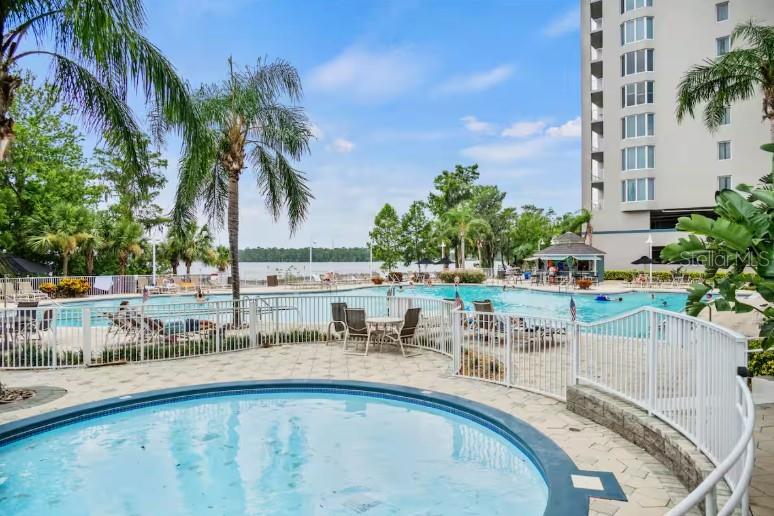 A circular hot tub sits in the foreground before a swimming pool and tall building — 13415 BLUE HERON BEACH DRIVE UNIT 403, ORLANDO, FL