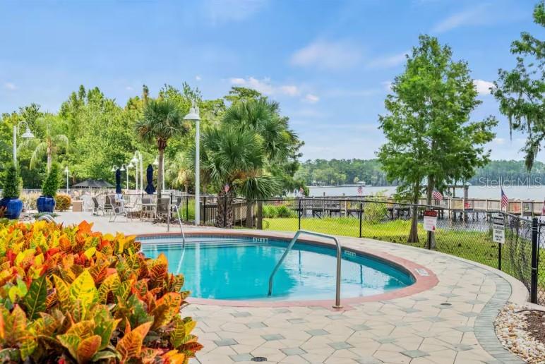 A small circular swimming pool sits on a paved patio overlooking a lake and dock — 13415 BLUE HERON BEACH DRIVE UNIT 403, ORLANDO, FL