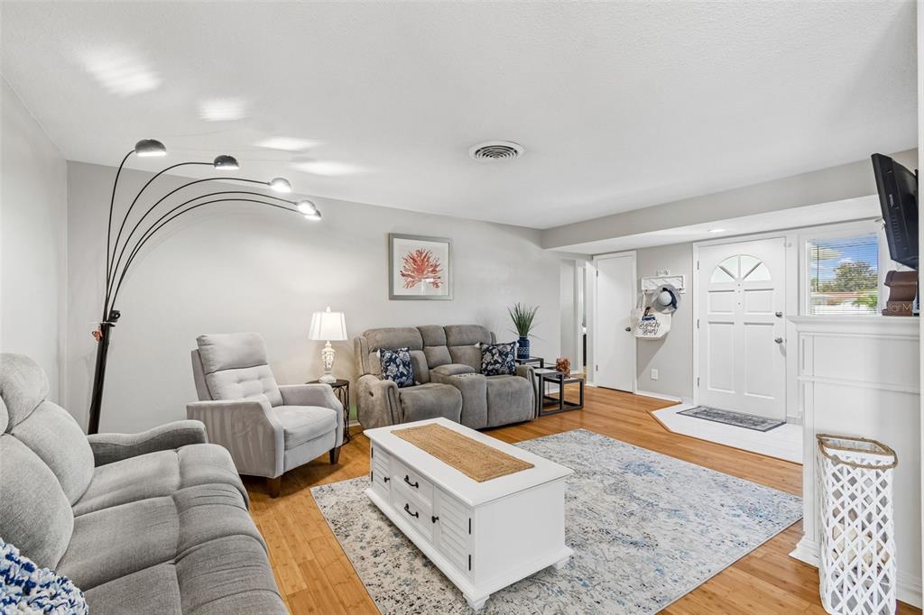 A living room features light gray walls, wood flooring, a sectional sofa, and a white coffee table — 1229 GRENADA AVENUE, CLEARWATER, FL