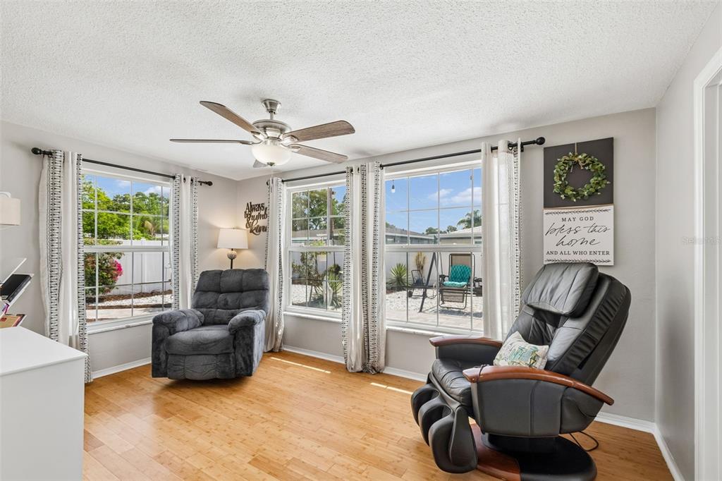 A living room features two armchairs, a ceiling fan, and windows overlooking a backyard patio — 1229 GRENADA AVENUE, CLEARWATER, FL