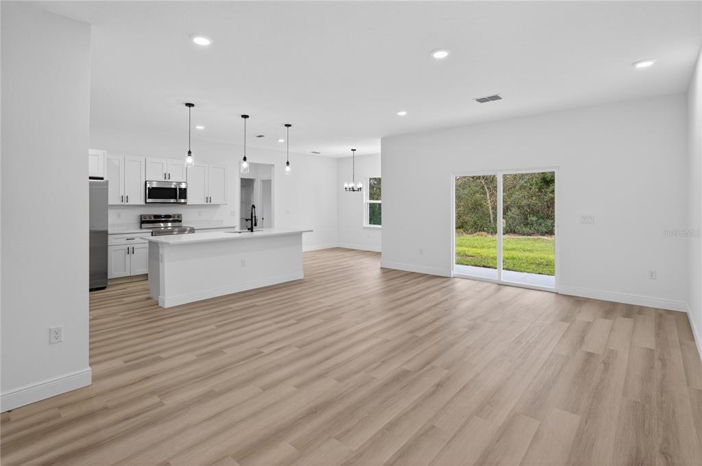 A bright, open-concept kitchen and living area featuring white cabinetry, light wood flooring, and sliding doors — 15028 SW 25TH CIRCLE, OCALA, FL